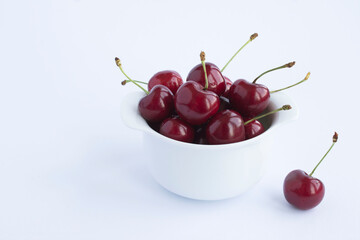 Wall Mural - Red cherries in the white bowl on the white background. Copy space. Closeup.
