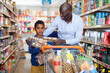 Happy friendly African family of father and tween son shopping together in supermarket