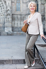 Wall Mural - Cheerful mature female is walking in classic jacket