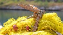Close Up Of Small Boat Anchor On Top Of Fishing Net With Blurred Background