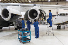 Maintenance Team Repairing Airplane Engine In Hangar
