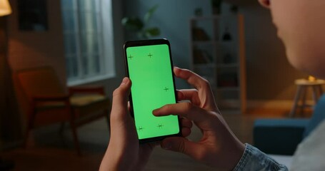 Wall Mural - Close up shot of guy using his smart phone with mock up green screen at night, using various gestures to scroll through online shop or social media 4k video template