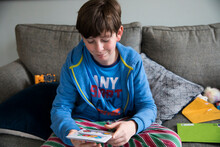 Smirking Teen Boy Reads Birthday Card While Sitting On Couch In Pjs