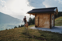 Father And Child From Back Walking In Mountains By Small Wooden House