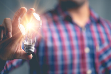 Poster - Idea innovation and inspiration concept.Hand of man holding illuminated light bulb, concept creativity with bulbs that shine glitter.Inspiration of ideas for sustainable business development.
