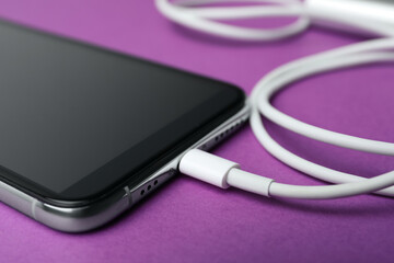 Smartphone and charge cable on purple background, closeup. Modern technology