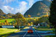 The car runs on a road with beautiful nature, high mountains and beautiful cities on the hills in the Austrian countryside. In autumn the trees turn yellow and orange.
