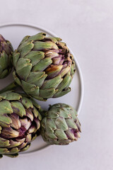 Topview image of artichokes in a white plate over light gray bac