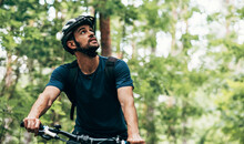Outdoor Image Of Handsome Cyclist Man Riding Bike In The Mountain. Male Athlete In Cycling Gear Practising Outside In The Forest On Nature Background. Travel And Extreme Sport Concept.