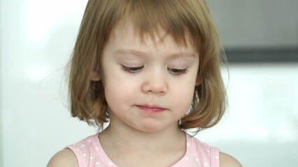 close up of little cute 3 years old child girl eats sweet pink cotton candy, looks at camera, smiles