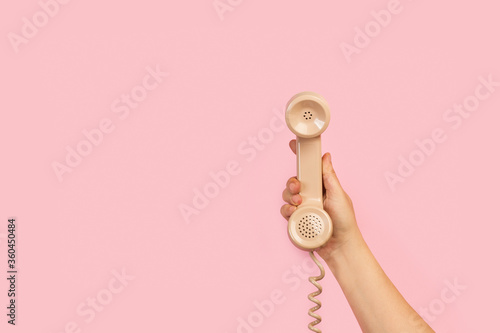 Fotografía Mano de mujer sosteniendo el tubo retro de un teléfono antiguo sobre fondo rosa liso y aislado