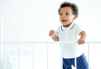 African American child boy stand near bed rail and he look happy by smiling and show teeth and look innocent. Concept of happiness emotion occur with good health and support from family.