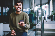 Happy Bearded Hipster Guy Excited With Good News Receiving Message On Smartphone Sitting On Urban Settings, Cheerful Handsome Man Satisfies With Mobile Tariffs For Calls And Messages Chatting On Phone