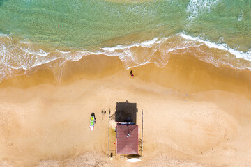 Wall Mural - Beach scene with Man walking by a lifeguard station and calm waves breaking on the beach, Top down aerial view.