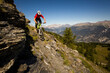 A mountain biker riding down a steep rocky trail in Bardonecchia, with blue sky and Italian alps behind.