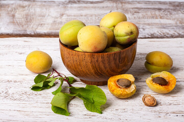 ripe organic apricots fruits in ash tree wooden bowl on a white wooden background