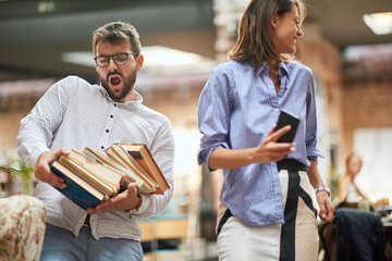 old-fashioned man carrying heavy pile of books that about to fall from his hands.  female with her cell phone in her hands looking away