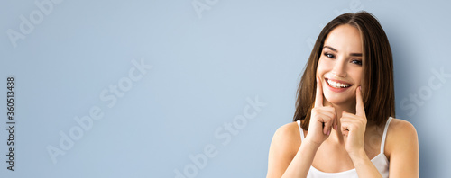 Cuadros en Lienzo Bright image of young brunette woman showing smile, in casual smart clothing, over grey background