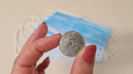 five shekels coin in female hand over surgical face protection masks