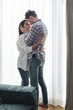 © LIGHTFIELD STUDIOS - Handsome man hugging beautiful girlfriend near window at home