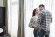 © LIGHTFIELD STUDIOS - Man kissing smiling girlfriend near window in living room