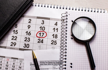 The calendar shows the day of tax payment. Nearby a magnifier, pen and notebook. Financial concept