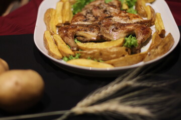 Chicken tabaka with fried potatoes and greens on a color background.