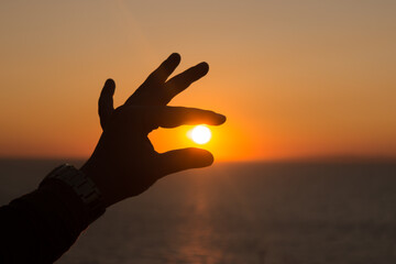 Woman hand silhouette catching the sun at sea and sunset landscape