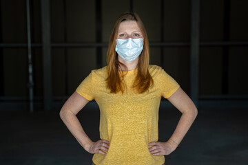 Woman standing with hands on her hips wearing surgical face mask to prevent spreading disease Covid-19. Dark background. Corona virus concept.