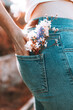 The girl stands with her back in blue jeans, flowers in her back pocket.