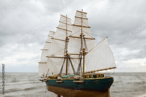 Antiquarian wooden scale model of the clipper tall ship, close-up. Dramatic sky and sea shore in the background. Traditional craft, souvenirs, hobby, collecting, vintage, modeling. Zero waste concept © Alex Stemmer
