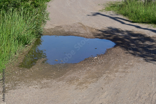 Dirt road with puddles in summer with grass side