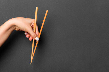 Wall Mural - Wooden chopsticks holded with female hands on black background. Ready for eating concepts with empty space