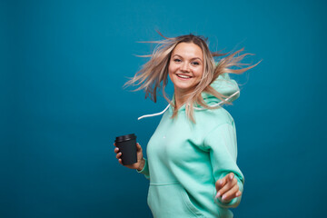 Wall Mural - Happy girl smiling and drinking coffee, portrait in Studio on blue background.