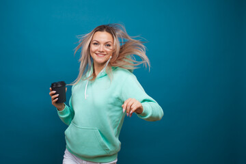 Wall Mural - Happy girl smiling and drinking coffee, portrait in Studio on blue background.