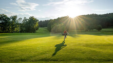 Handsome Young Golfer Carrying A Bag And Walking To The Next Hole On A Golf Course On A Beautiful Sunset In The Background. Sport Playground For Golf Club Concept 