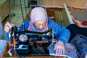 Wall Mural - Arabic muslim old woman using old sewing machine