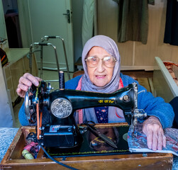 Wall Mural - Arabic muslim old woman using old sewing machine