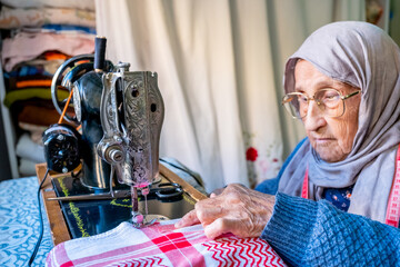 Wall Mural - Arabic muslim old woman using old sewing machine