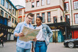 © BullRun - African american young woman together with caucasian friend holding map and searching right direction of route standing on street in urban setting.Trip of multicultural couple in love in new city