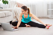 © Admiral - Online home stretching. Slim girl doing fitness routine on floor and watching laptop at home. Copy space