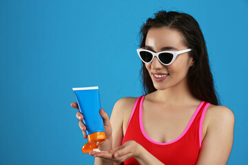 Wall Mural - Young woman applying sun protection cream on dark blue background