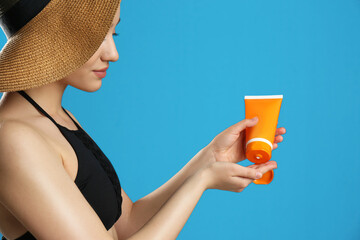 Wall Mural - Young woman applying sun protection cream on blue background, closeup