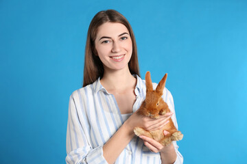 Wall Mural - Young woman with adorable rabbit on blue background. Lovely pet