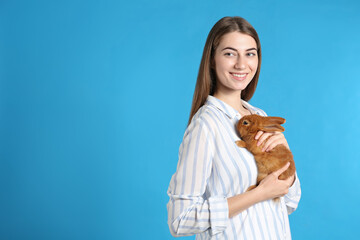 Canvas Print - Young woman with adorable rabbit on blue background, space for text. Lovely pet