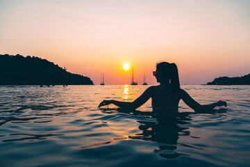 Wall Mural - Silhouette of Travel asian woman relax on sea beach in sunset Thailand