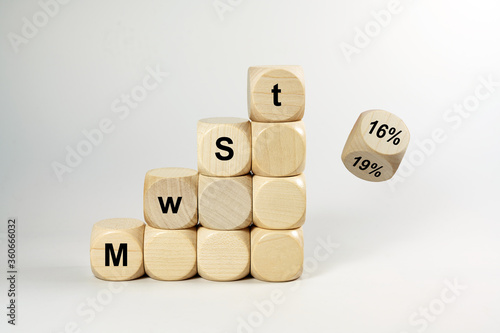 MwSt (value added tax) written on wooden dices, one is falling and turns from 19% to 16%, finance concept, German economic stimulus package after the coronavirus pandemic, gray background, copy space