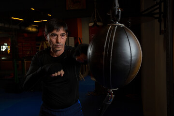 A black-haired miA black-haired middle-aged man in a black rashguard is Boxing with a leather boxer bag.ddle-aged man in a black rashguard is Boxing with a leather boxer bag. High quality photo