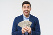 © Damir Khabirov - Wow! I won! Young man shouting with excitement because he won prize in lottery, holding dollars in cash, shocked and happy, isolated on gray background