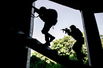 Two military soldiers in camouflage storm the building climbing the stairs